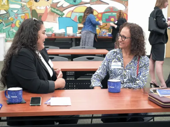 Two women chat at a table with FORGE mugs in front of them