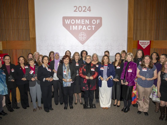 A group of women holding their awards pose for a photo in front of a projector screen.