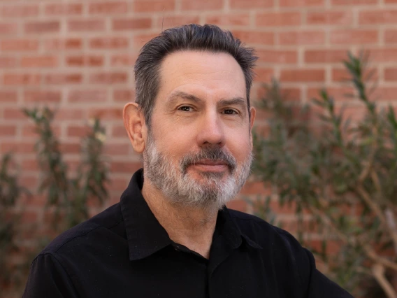 Image of gray-bearded man in black shirt in front of brick wall