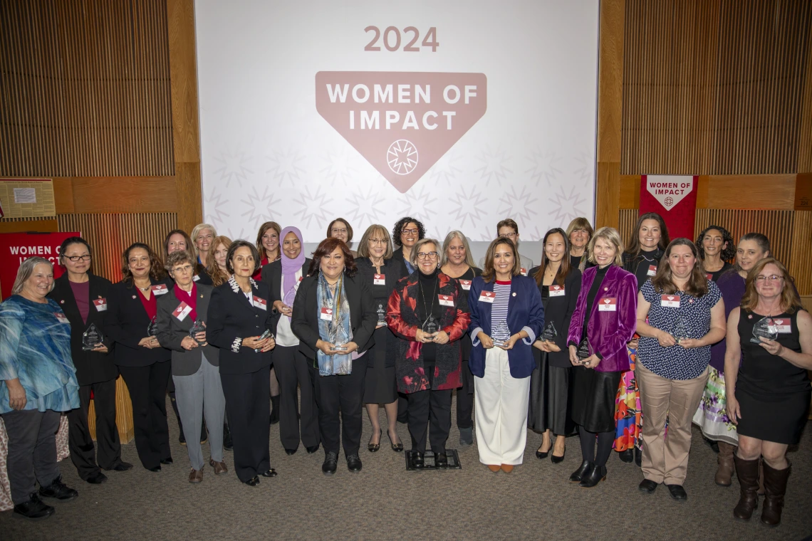 A group of women holding their awards pose for a photo in front of a projector screen.