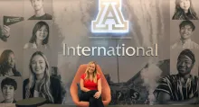 An intern sits in front of a sign for Arizona International